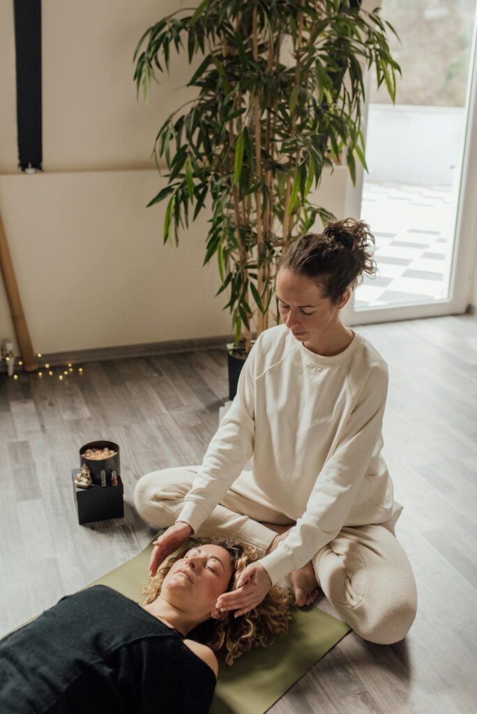 A calming scene depicting a woman practicing Reiki therapy on another woman lying on a yoga mat indoors.